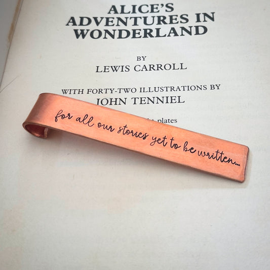 A copper bookmark with text stamped on saying 'for all our stories are yet to be written'
