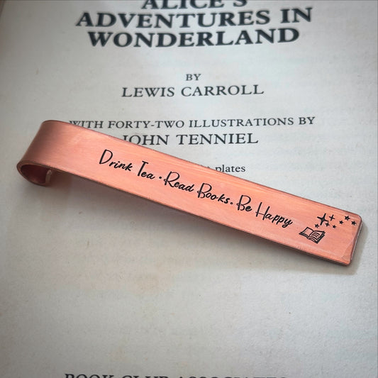 A copper hand stamped bookmark gift with the text 'DRINK TEA. READ BOOKS. BE HAPPY.'