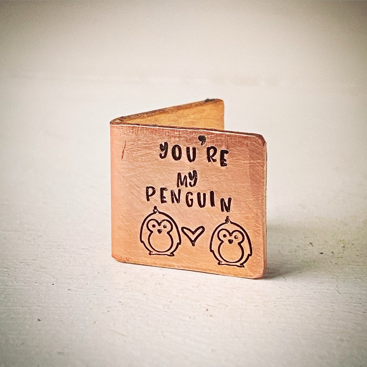 a small bronze-colored keepsake card with the text 'You're my PENGUIN' and two stylized penguin figures stamped on it.