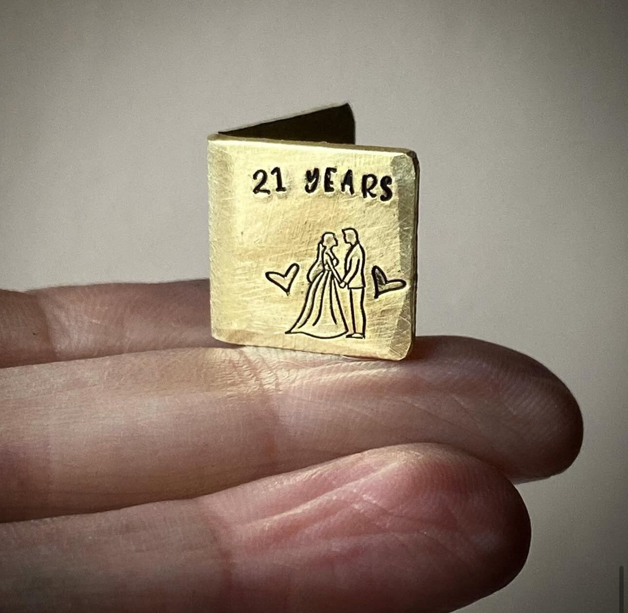 A personalized miniature brass card with '21 YEARS' and an illustration of a couple embracing, along with heart shapes.
