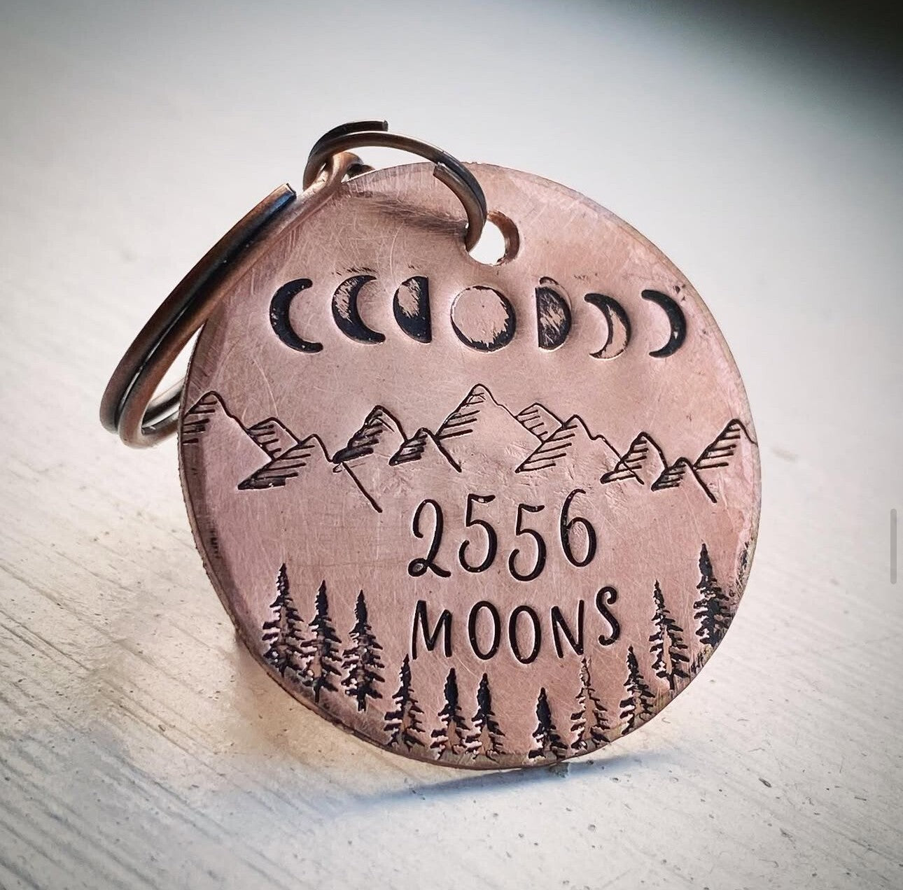 A copper keychain gift with engraved moon phases and the text '2556 Moons', symbolizing a 7th wedding anniversary gift.