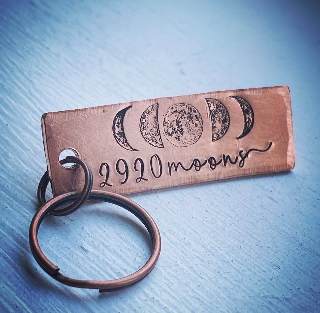 A bronze keychain with the text '2020 moons' and illustrations of moons in different phases engraved on it.