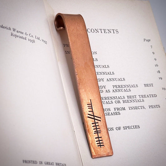 A bronze bookmark with the word 'eight' hand stamped in ogham script.