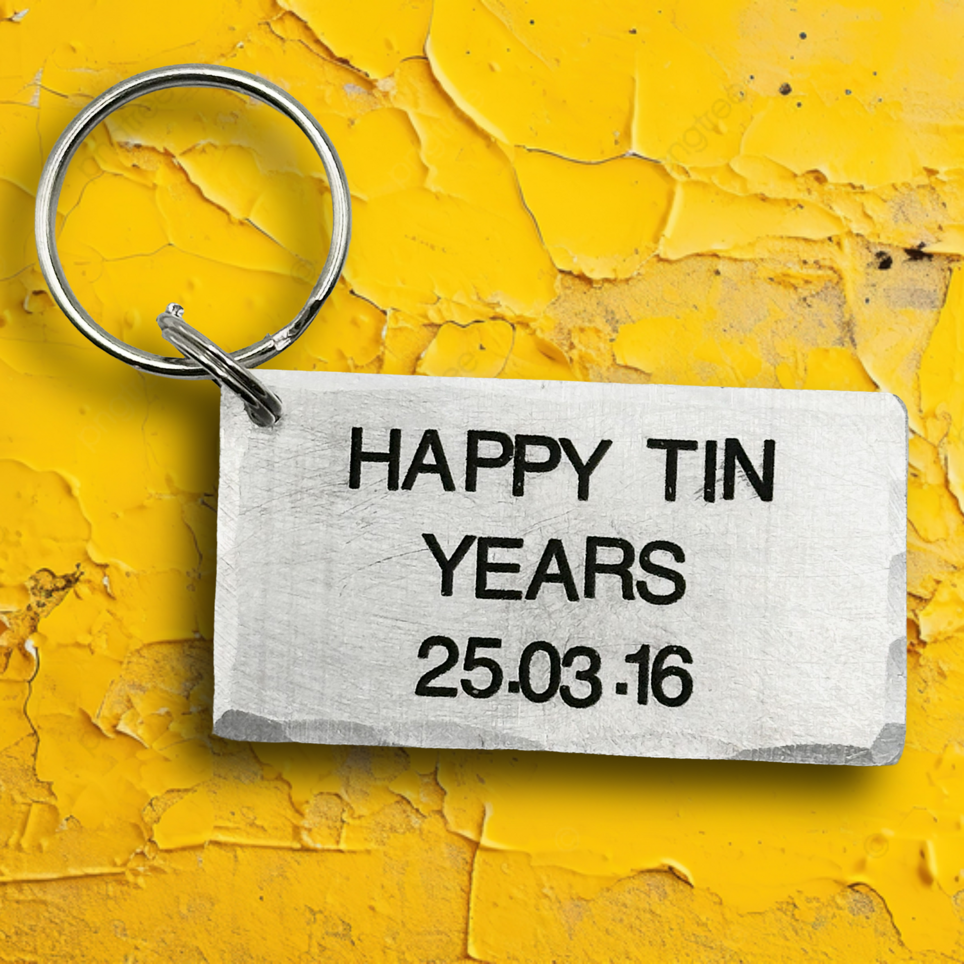 Keychain with 'Happy Tin Years 25.03.16' text on a yellow textured background
