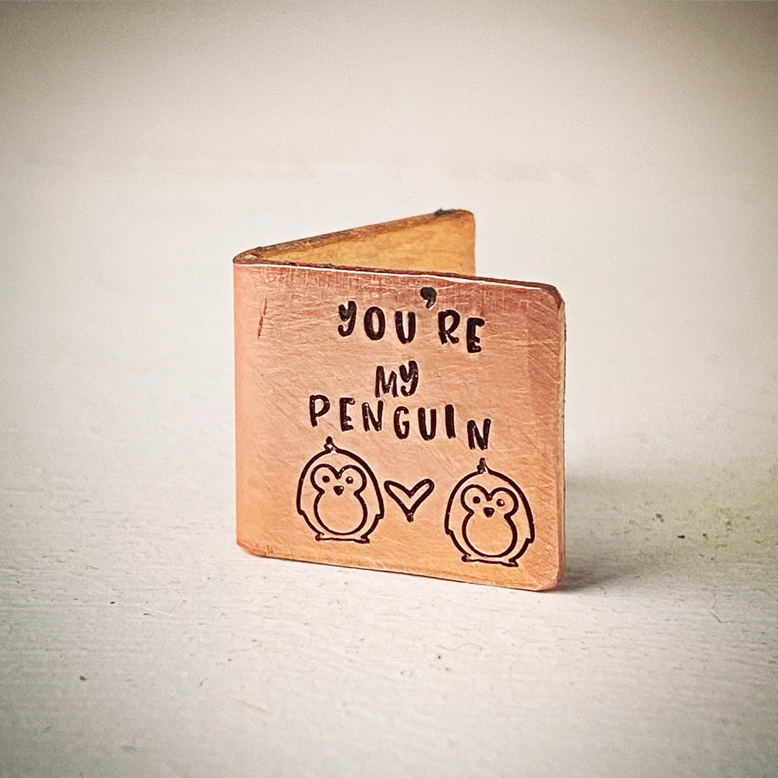 a small bronze-colored keepsake card with the text 'You're my PENGUIN' and two stylized penguin figures stamped on it.