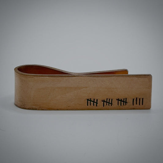 A bronze metal money clip with engraved tally marks.