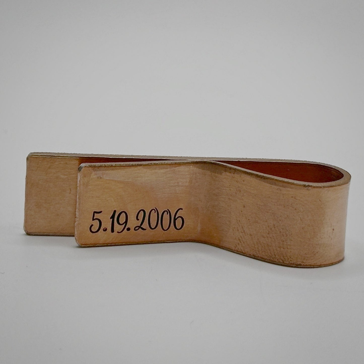A bronze metal money clip with an engraved date