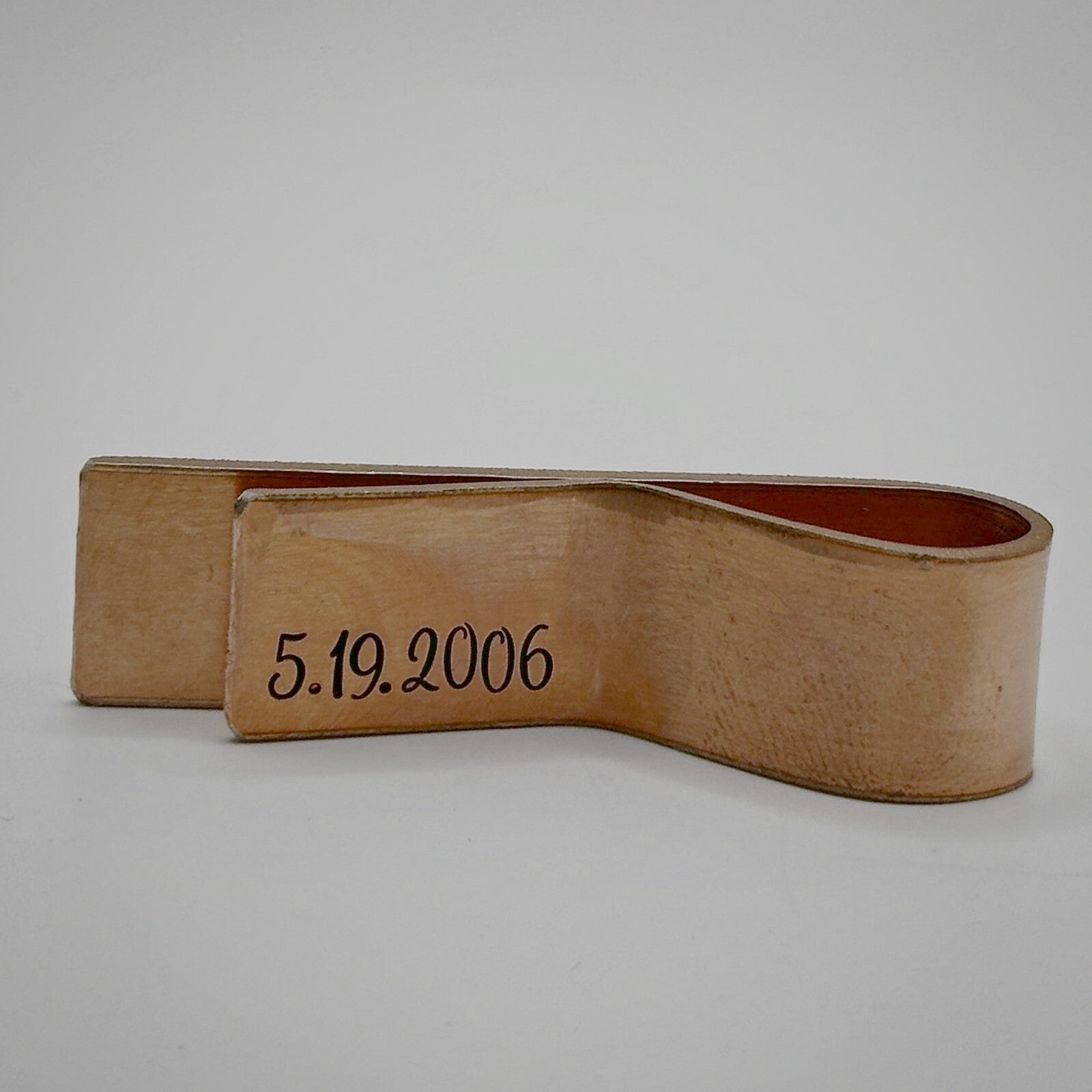A bronze metal money clip with an engraved date