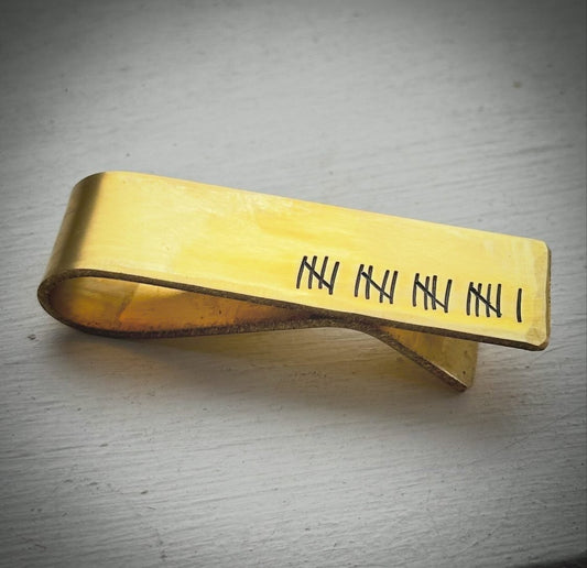 A personalized brass money clip with engraved tally marks.