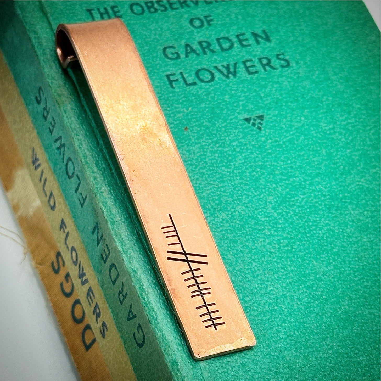 A bronze bookmark with the word 'eight' hand stamped in ogham script.
