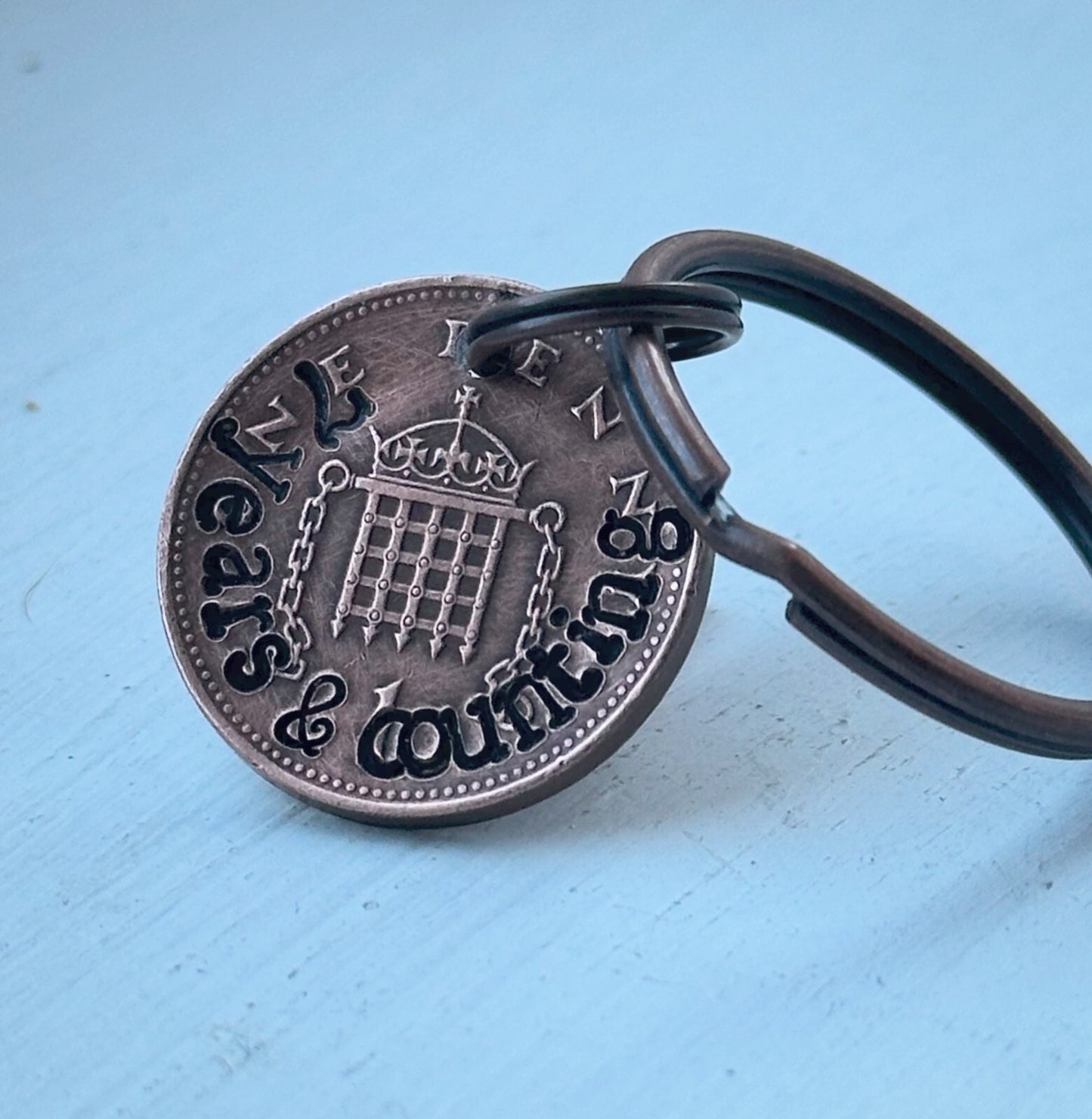 A keychain featuring a hand-stamped copper coin with the inscription '7 years and counting' and a crown motif at the center.