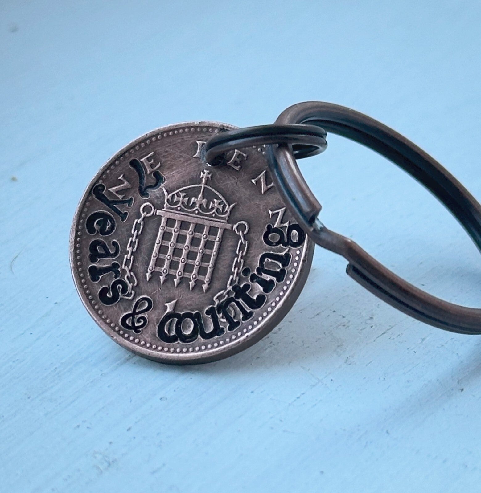 A keychain featuring a hand-stamped copper coin with the inscription '7 years and counting' and a crown motif at the center.