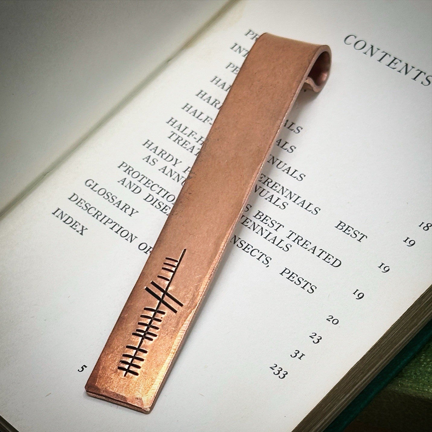 A bronze bookmark with the word 'eight' hand stamped in ogham script.