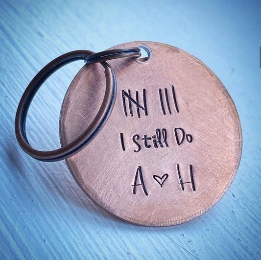 A copper keychain with the inscription 'I still do' along with custom initials stamped.