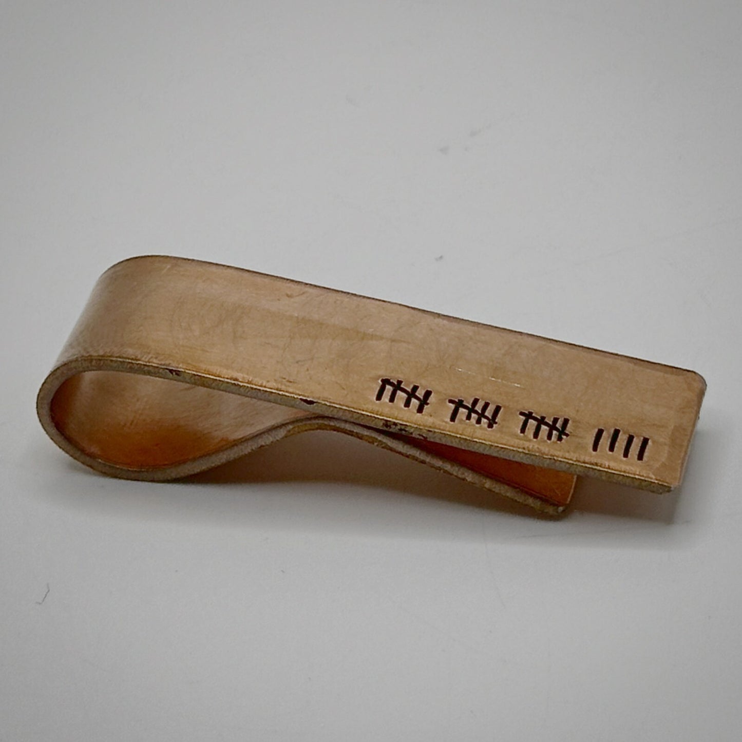 A bronze metal money clip with engraved tally marks.
